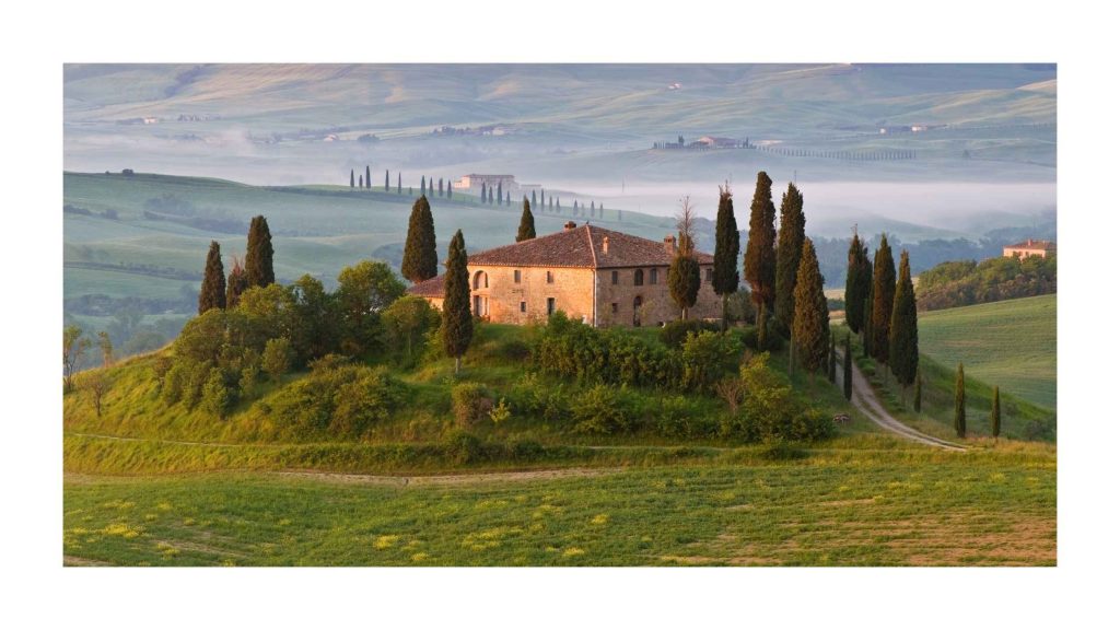 Paisagem da Toscana com colinas verdes, ciprestes e construção rural italiana, referência estética para casamento estilo toscana.